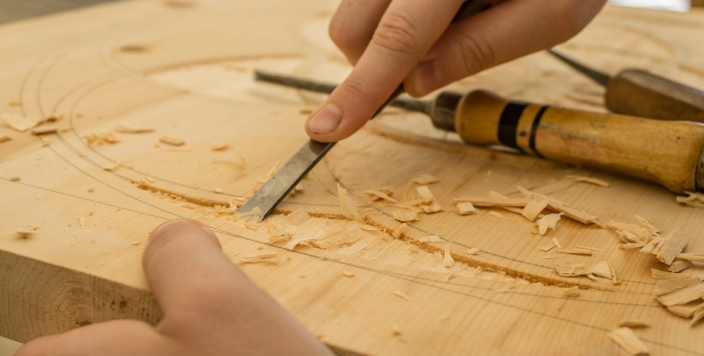 Mains de l’artisan guidant un ciseau à bois dans une planche, entourées de copeaux
